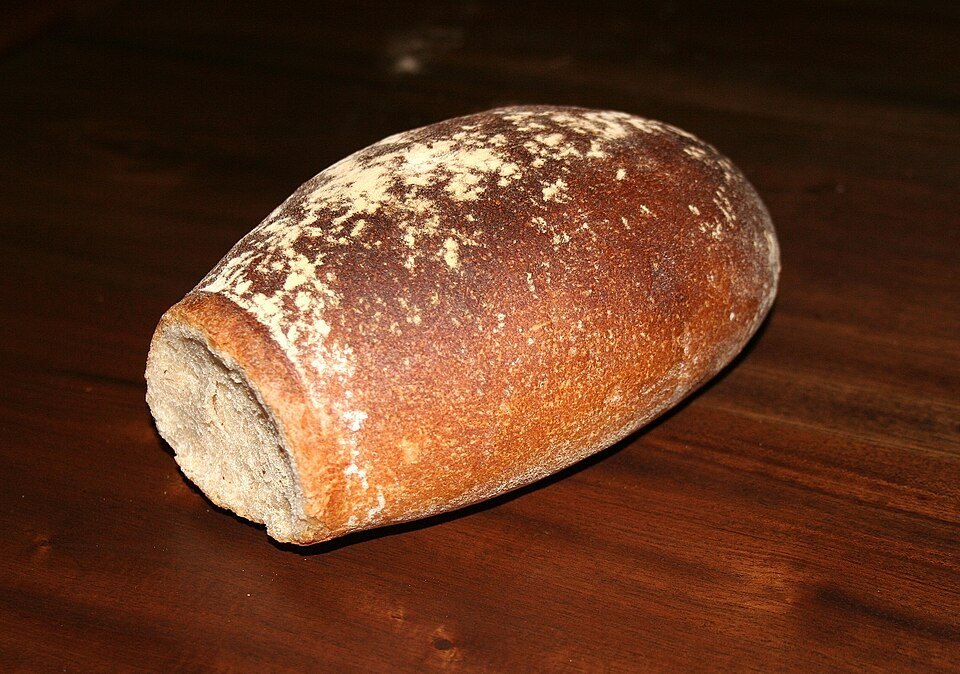 Photographie illustrative : Pain bâlois rustique à la croûte foncée, posé sur une table en bois.